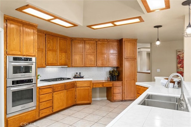 kitchen featuring tile countertops, brown cabinets, pendant lighting, and a sink