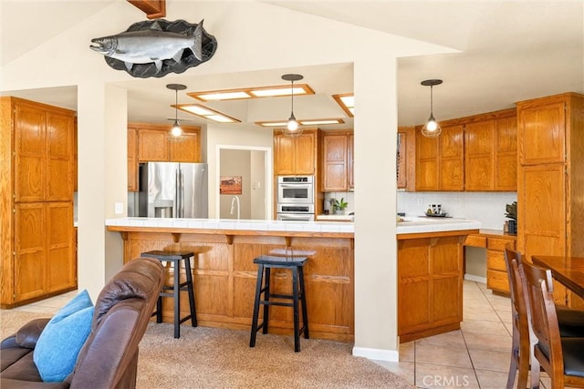 kitchen featuring a peninsula, hanging light fixtures, appliances with stainless steel finishes, brown cabinets, and a kitchen bar