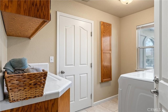 washroom with light tile patterned floors, washer / clothes dryer, cabinet space, and baseboards