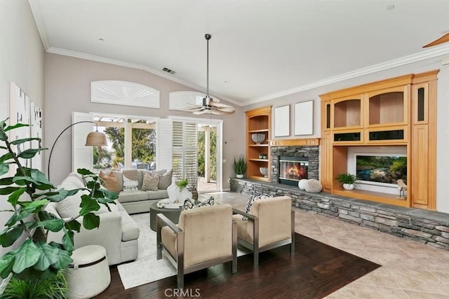 tiled living area with visible vents, ceiling fan, vaulted ceiling, crown molding, and a stone fireplace