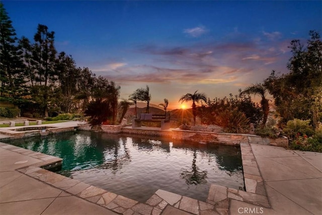 pool at dusk with a pool with connected hot tub and a patio area