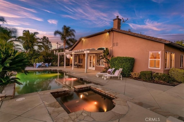 back of house at dusk featuring an in ground hot tub, stucco siding, a patio area, and a pergola