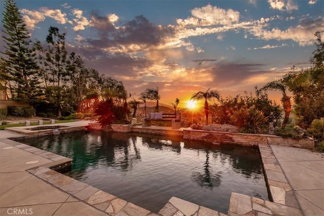 pool at dusk with a pool with connected hot tub and a patio