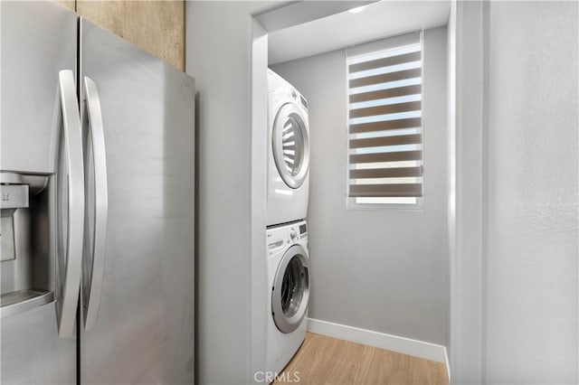 laundry room featuring baseboards, laundry area, light wood-style flooring, and stacked washer / drying machine