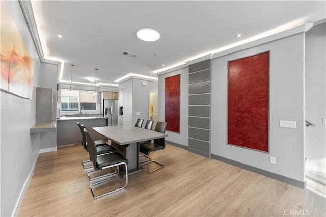 dining room with ornamental molding, light wood-style flooring, visible vents, and baseboards