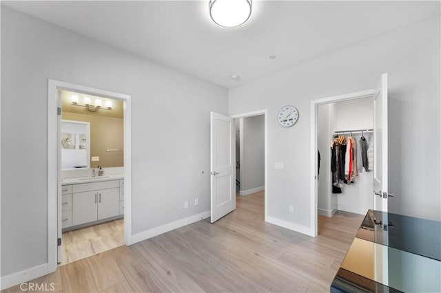 bedroom with a sink, baseboards, a closet, light wood-type flooring, and a walk in closet