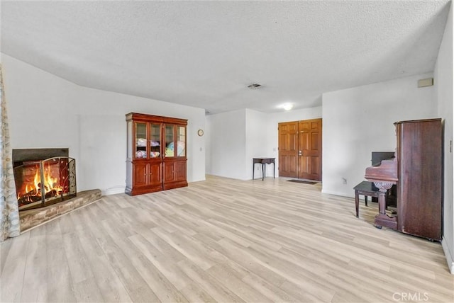 unfurnished living room featuring a warm lit fireplace, visible vents, light wood-style flooring, and a textured ceiling