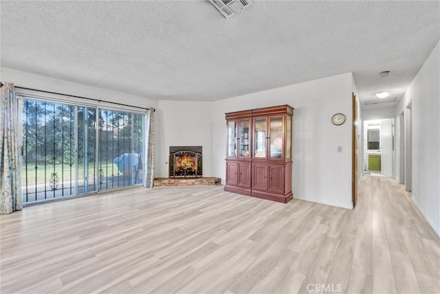 unfurnished living room with a textured ceiling, a lit fireplace, light wood finished floors, and visible vents