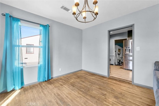 empty room with baseboards, light wood finished floors, visible vents, and a notable chandelier