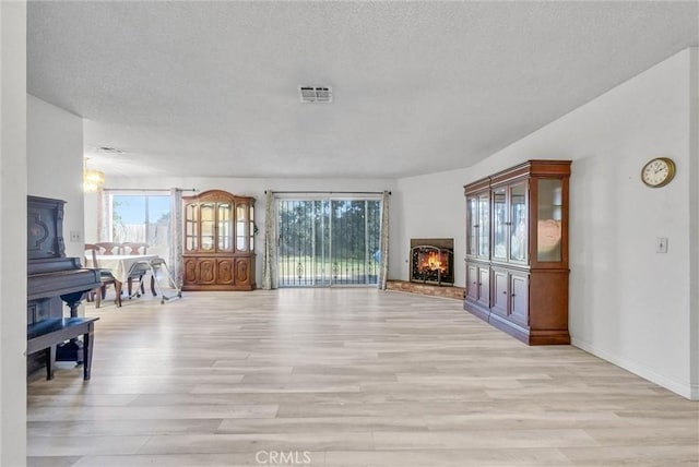 unfurnished living room featuring light wood-type flooring, a warm lit fireplace, visible vents, and a textured ceiling