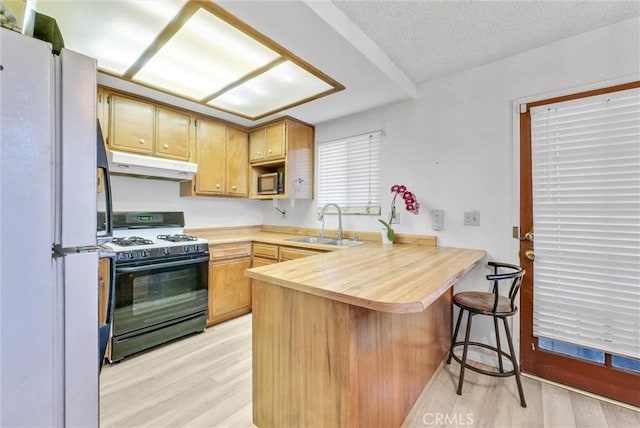 kitchen with gas range oven, light countertops, a sink, a peninsula, and under cabinet range hood