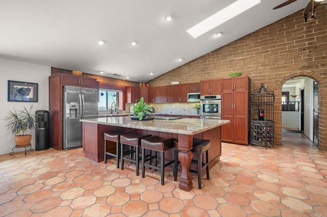 kitchen featuring light stone counters, a skylight, a large island, stainless steel appliances, and a kitchen breakfast bar