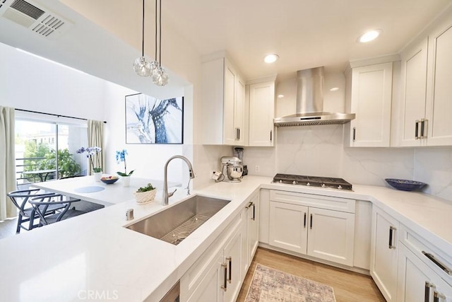 1617 S Beverly Glen Blvd Unit 303, Los Angeles, CA 90024 - kitchen featuring a sink, wall chimney range hood, stainless steel gas stovetop, light wood-style flooring, and light countertops