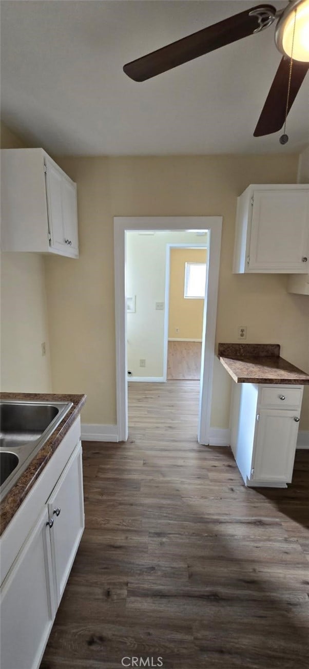 kitchen with baseboards, white cabinets, a ceiling fan, dark countertops, and wood finished floors