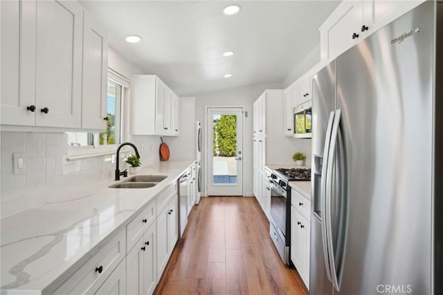 kitchen with plenty of natural light, white cabinets, light stone countertops, stainless steel appliances, and a sink