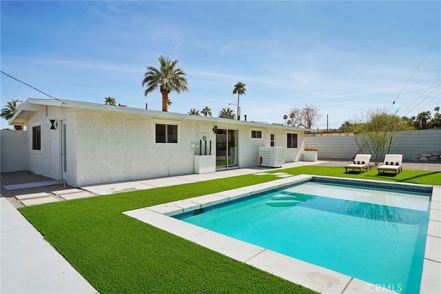 rear view of property with a lawn, a fenced backyard, a fenced in pool, and stucco siding