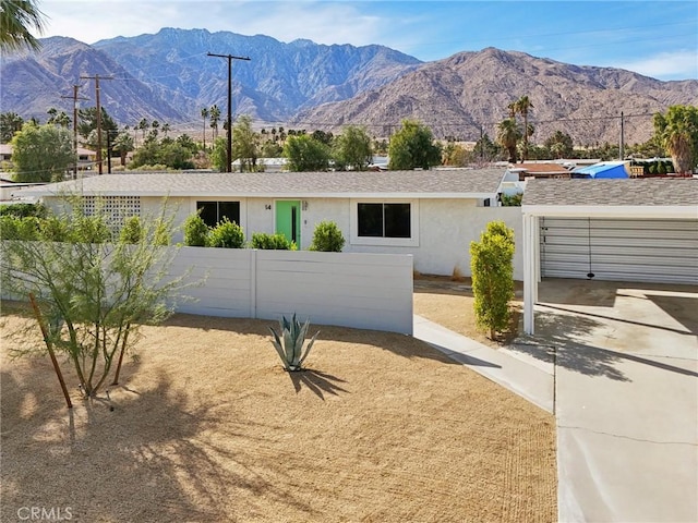 ranch-style home with a fenced front yard, stucco siding, a mountain view, a garage, and driveway