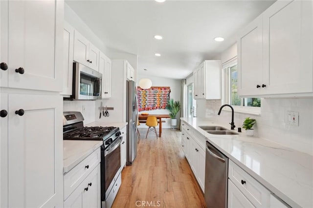 kitchen featuring light stone counters, appliances with stainless steel finishes, white cabinetry, a sink, and light wood-type flooring