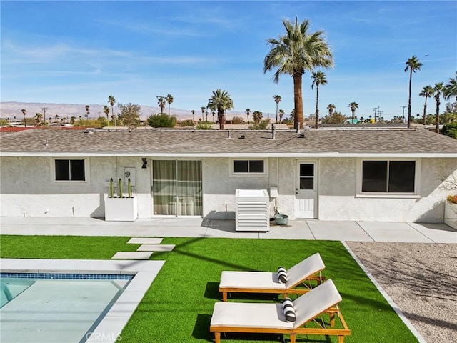 rear view of house with roof with shingles, a patio area, a lawn, and stucco siding