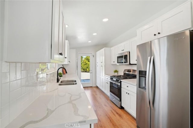 kitchen with light stone countertops, white cabinetry, appliances with stainless steel finishes, and a sink