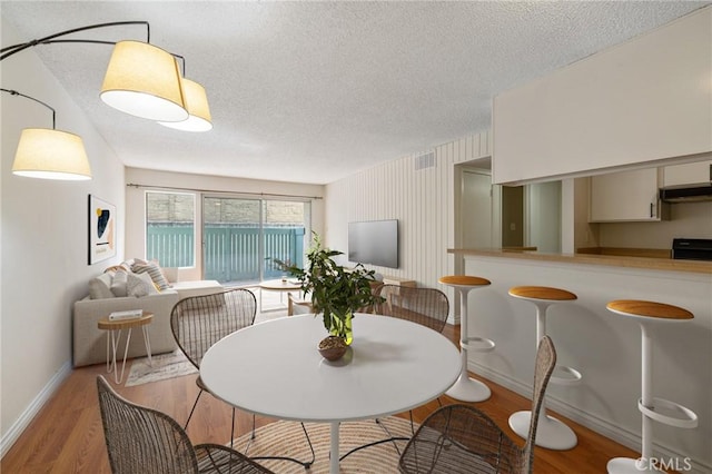 dining space featuring baseboards, a textured ceiling, visible vents, and wood finished floors