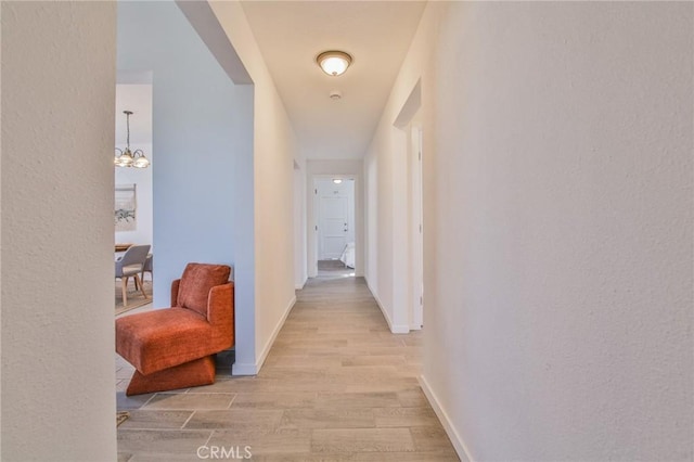 hall featuring light wood-type flooring, an inviting chandelier, and baseboards