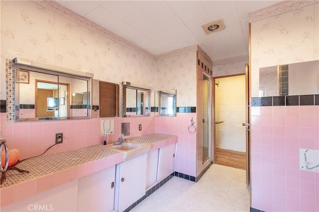 bathroom featuring wallpapered walls, a stall shower, wainscoting, vanity, and tile walls