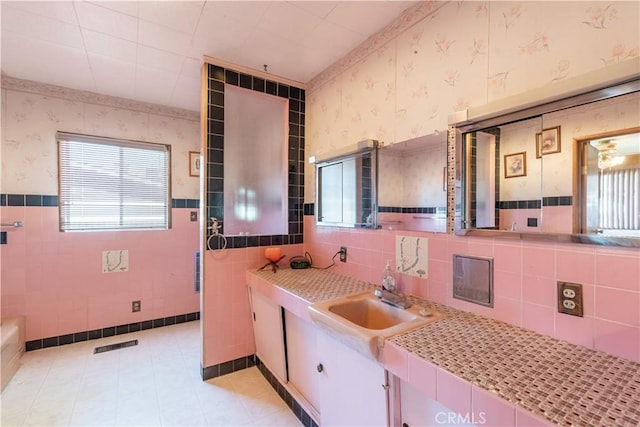 bathroom with wallpapered walls, tile walls, and a wainscoted wall