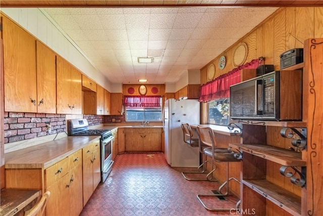 kitchen with dark floors, light countertops, freestanding refrigerator, brown cabinets, and gas range