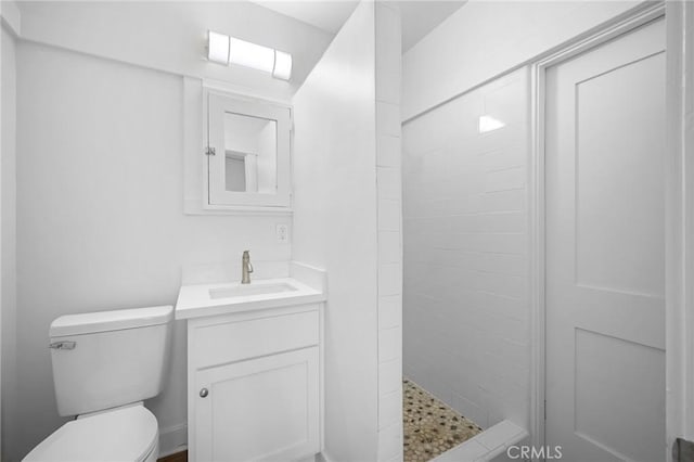 bathroom with toilet, a tile shower, and vanity