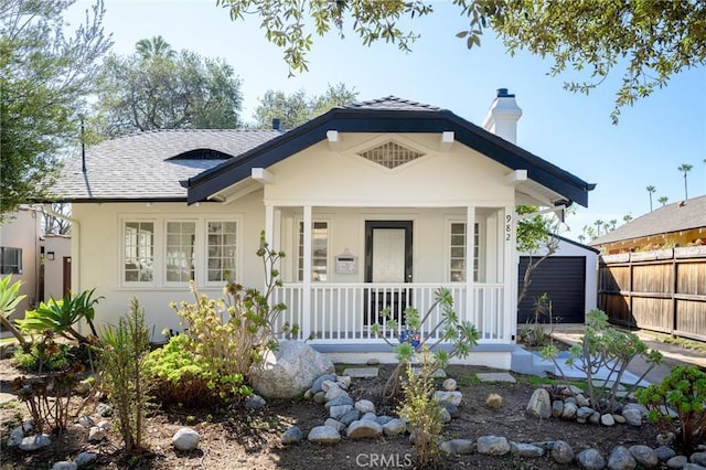 view of front facade with a porch, a shingled roof, fence, stucco siding, and a chimney