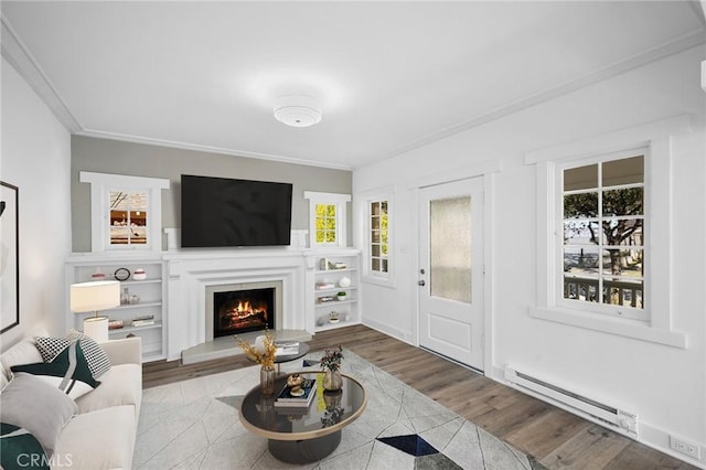 living area with a baseboard heating unit, ornamental molding, a lit fireplace, and wood finished floors