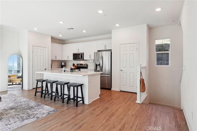 kitchen with an island with sink, stainless steel appliances, light countertops, a kitchen bar, and white cabinetry