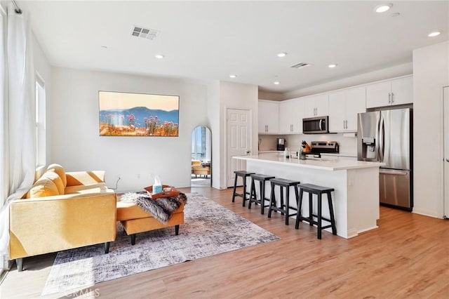 kitchen with a breakfast bar area, stainless steel appliances, light countertops, a kitchen island with sink, and white cabinetry