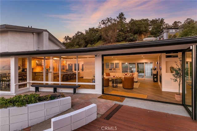 back of house at dusk with a deck and stucco siding