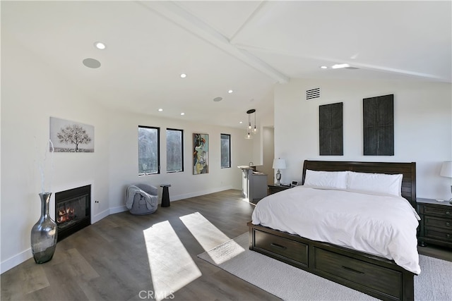 bedroom with vaulted ceiling with beams, wood finished floors, visible vents, baseboards, and a glass covered fireplace