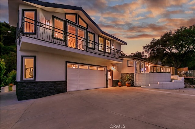 view of front of property featuring a garage, stone siding, a balcony, and stucco siding