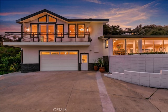 view of front facade with a garage, stone siding, a balcony, and stucco siding