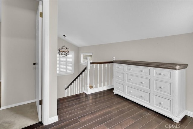 hall with baseboards, dark wood finished floors, vaulted ceiling, an upstairs landing, and a notable chandelier