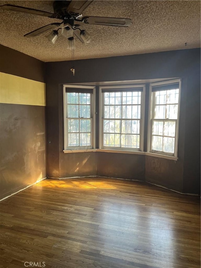 unfurnished room with a textured ceiling, a ceiling fan, and wood finished floors