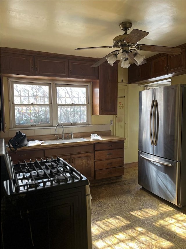 kitchen featuring black gas range, ceiling fan, freestanding refrigerator, light floors, and a sink