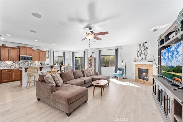 living room with ceiling fan, a fireplace, light wood-style flooring, and recessed lighting