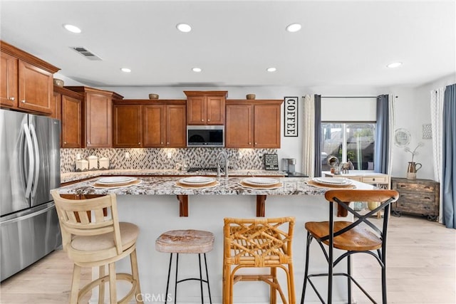 kitchen featuring appliances with stainless steel finishes, a center island with sink, and light stone counters