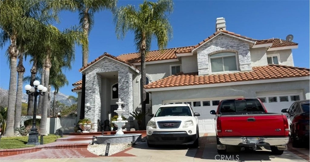 mediterranean / spanish home with stucco siding, concrete driveway, a chimney, and a tile roof