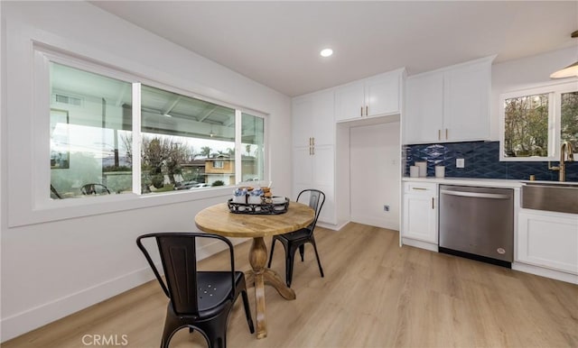 kitchen with white cabinets, light countertops, light wood-type flooring, backsplash, and dishwasher