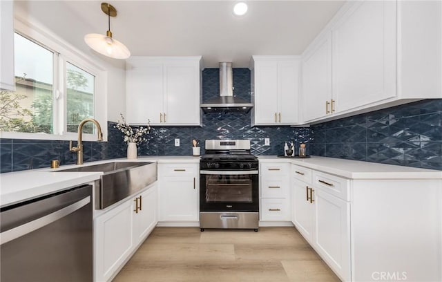 kitchen featuring decorative light fixtures, stainless steel appliances, light countertops, a sink, and wall chimney range hood