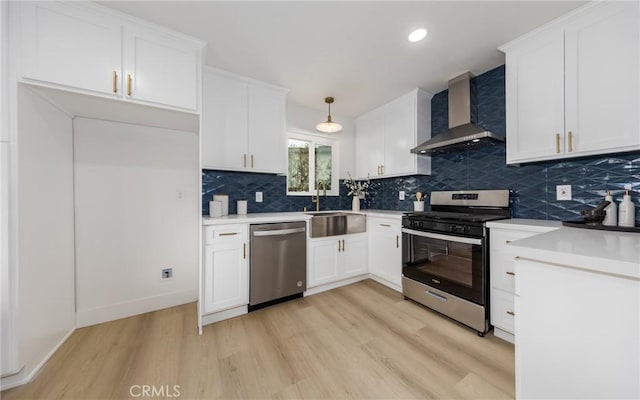 kitchen with stainless steel appliances, wall chimney range hood, hanging light fixtures, and white cabinets