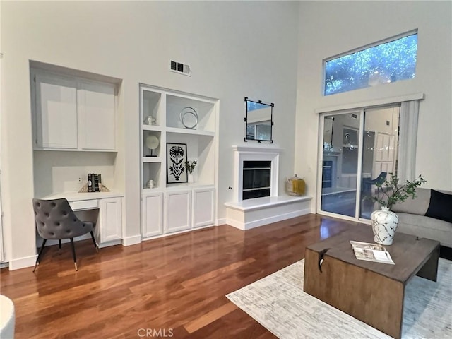 living area with built in features, wood finished floors, visible vents, built in study area, and a glass covered fireplace