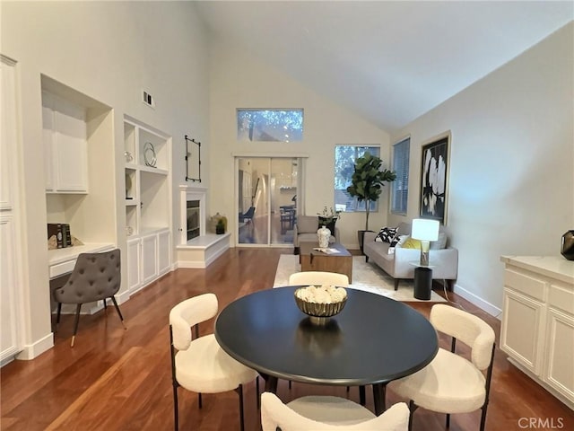 dining space with built in features, visible vents, dark wood-style flooring, vaulted ceiling, and a glass covered fireplace