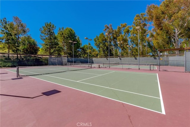 view of tennis court featuring community basketball court and fence